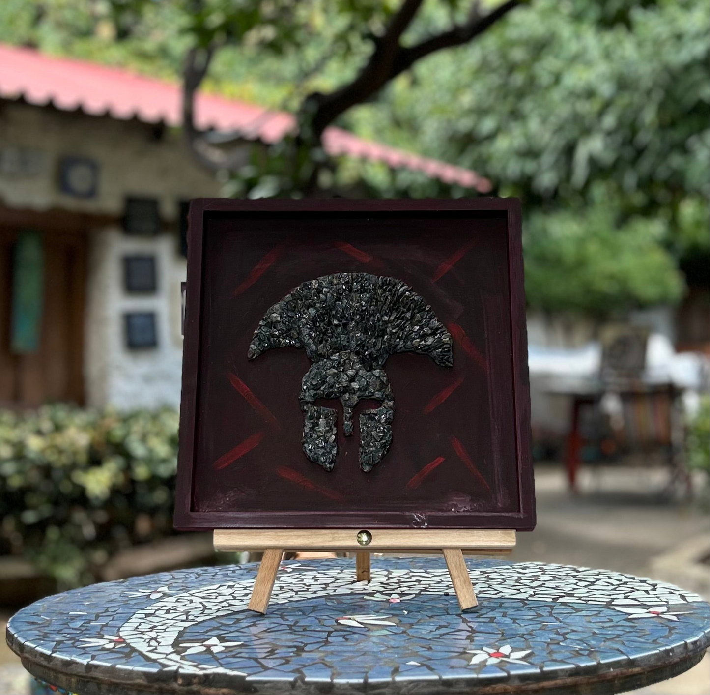 Decorative wall art of spartan warrior helmet.  Materials used are black stone on wooden based frame.