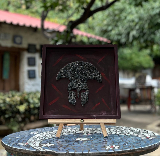 Decorative wall art of spartan warrior helmet.  Materials used are black stone on wooden based frame.